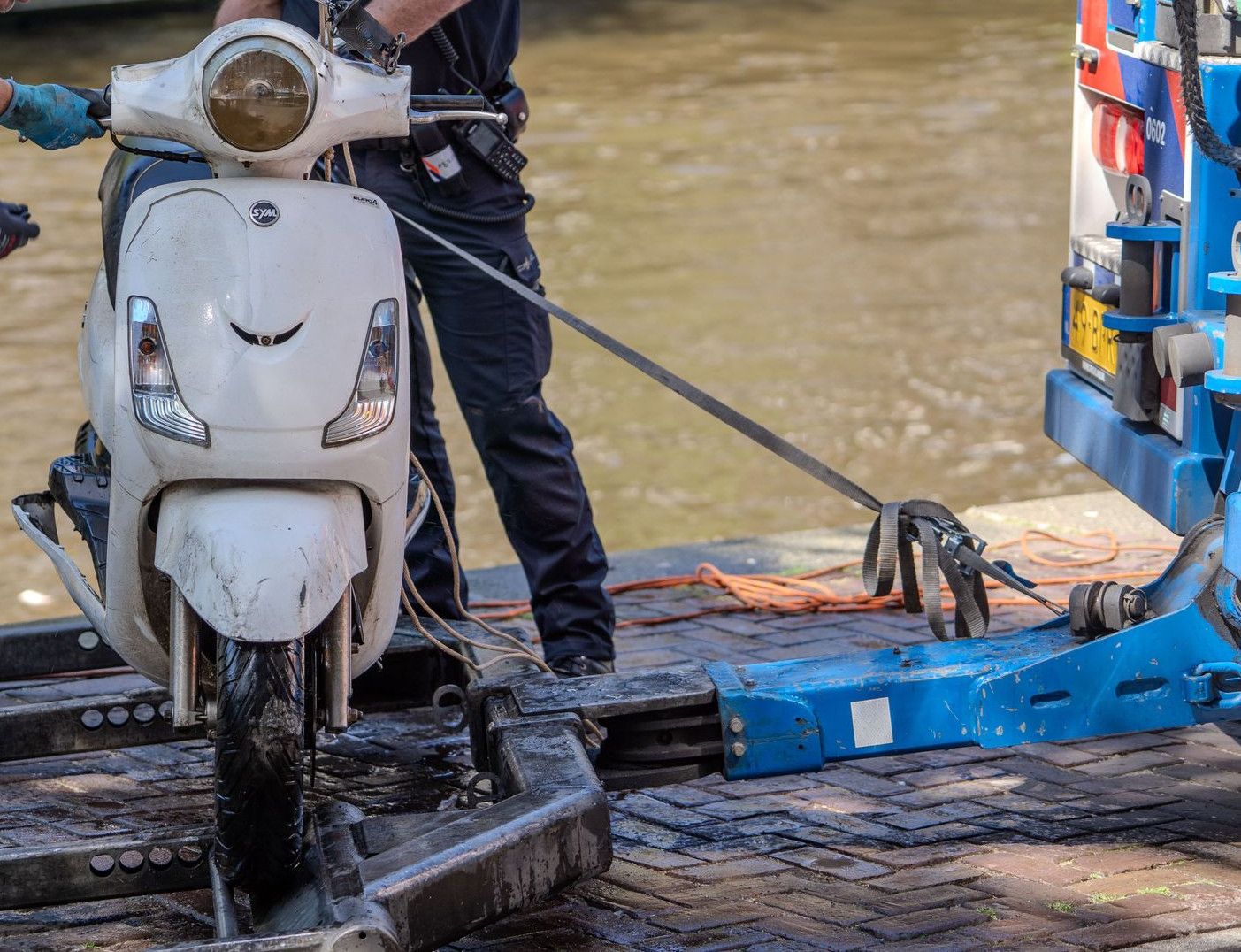 Police officers retrieve a motor scooter from a canal using towing equipment.